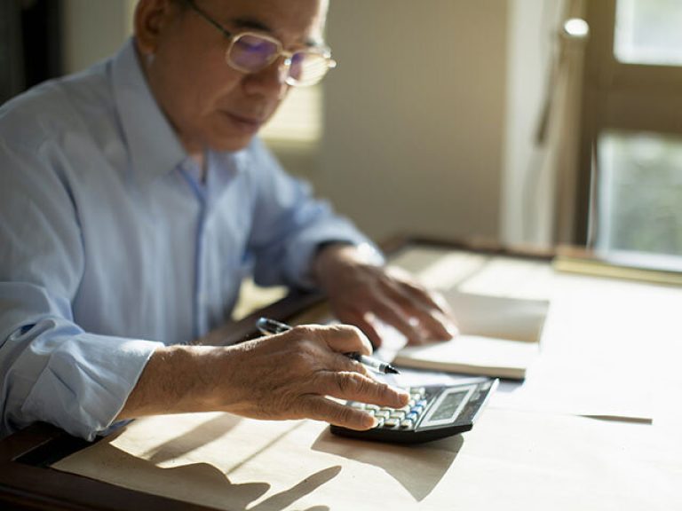 Taiwanese senior man sitting at table and calculating finances